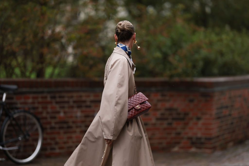 COPENHAGEN, DENMARK - AUGUST 09: Guest seen outside Skall Studio show wearing golden earrings, blue Chanel silk scarf, crocheted light yellow top, beige oversized trenchcoat, burgundy colored Chanel Classic Flap Bag, red Gucci logo socks and brow clogs during the Copenhagen Fashion Week Spring/Summer 2024 on August 09, 2023 in Copenhagen, Denmark. (Photo by Jeremy Moeller/Getty Images)