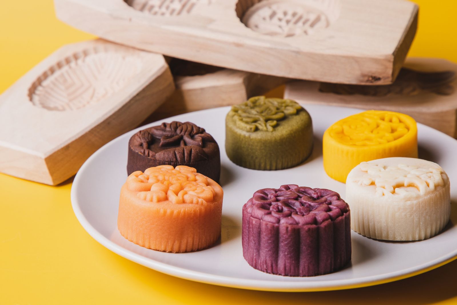 a plate full of mooncakes with exquisite flora pattern and different kind of wood mooncake molds against yellow background