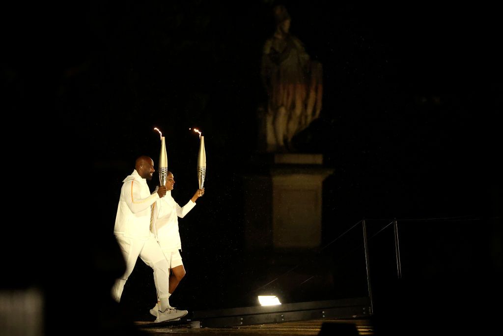 PARIS, FRANCE - JULY 26: Torch bearers French Athlete Marie-Jose Perec and French Judo Practitioner Teddy Riner walk to light the Olympic Cauldron at the Gardens of the Tuileries during the opening ceremony of the Olympic Games Paris 2024 on July 26, 2024 in Paris, France. (Photo by Carl Recine/Getty Images)