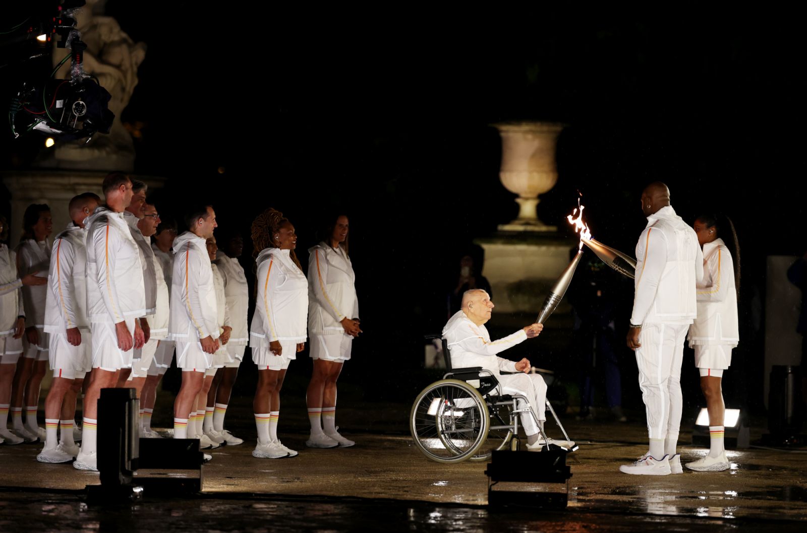 PARIS, FRANCE - JULY 26: Torch bearer Charles Coste (C) passes the torch to French Athlete Marie-Jose Perec (R) and French Judo Practitioner Teddy Riner (2nd R) walk to light the Olympic Cauldron at the Gardens of the Tuileries during the opening ceremony of the Olympic Games Paris 2024 on July 26, 2024 in Paris, France. (Photo by Al Bello/Getty Images)