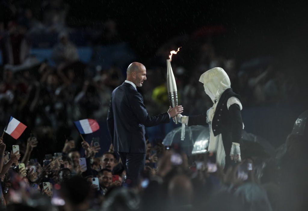 PARIS, FRANCE - JULY 26: French former football player Zinedine Zidane (L) holds the Olympic flame at the Trocadero during the opening ceremony of the Paris 2024 Olympic Games in Paris on July 26, 2024. (Photo by Mustafa Ciftci/Anadolu via Getty Images)