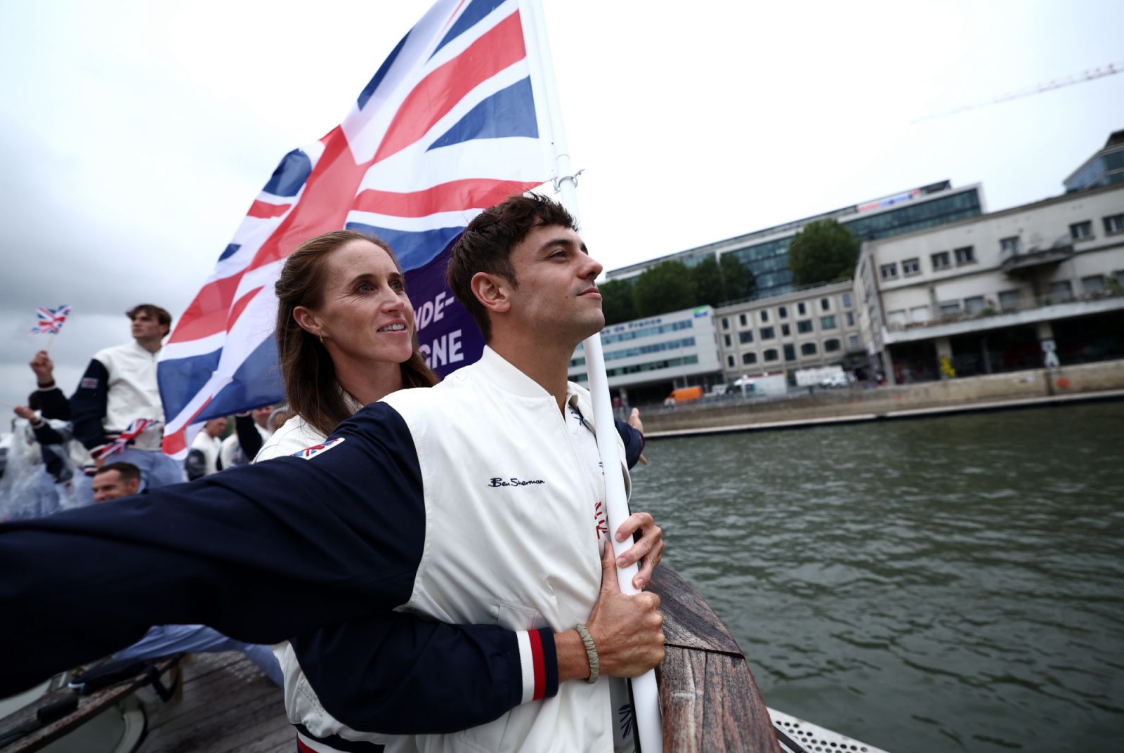 PARIS, FRANCE - JULY 26: Thomas Daley, Helen Glover, Flagbearers of Team Great Britain, gesture on a boat while holding the national flag on the River Seine during the opening ceremony of the Olympic Games Paris 2024 on July 26, 2024 in Paris, France. (Photo by Naomi Baker/Getty Images)