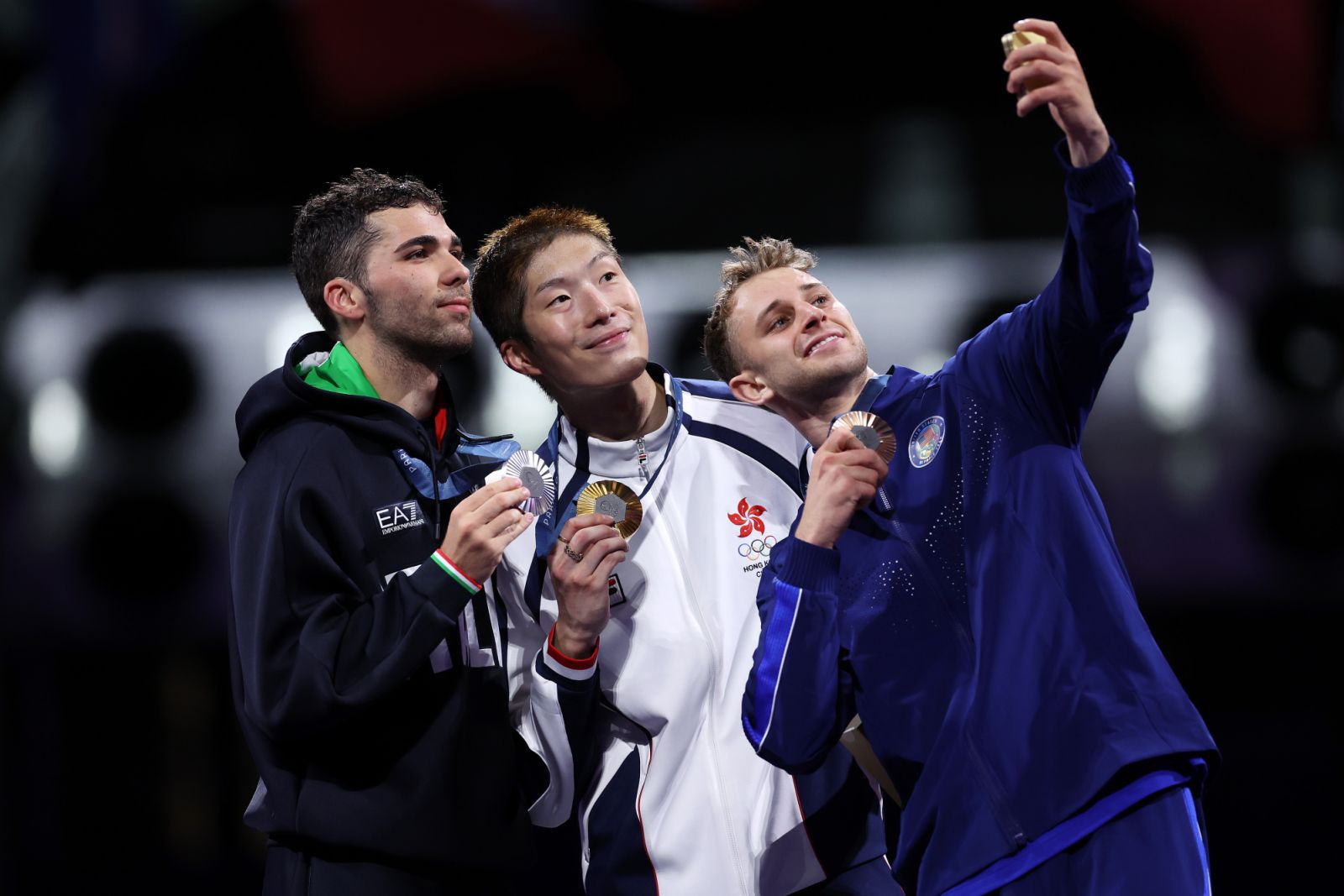 PARIS, FRANCE - JULY 29: Ka Long Cheung of team Hong Kong (C), Silver medalist Filippo Macchi of team Italy (L) and Bronze medalist Nick Itkin of United States(R) take a selfie on the podium during the Men's Foil Individual medal ceremony on day three of the Olympic Games Paris 2024 at Grand Palais on July 29, 2024 in Paris, France. (Photo by Carl Recine/Getty Images)