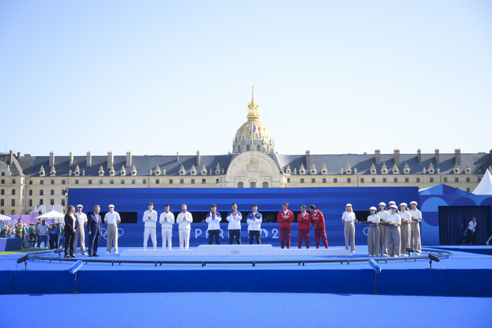 PARIS, FRANCE - JULY 29: Team South Korea (blue) in the first place, team France (white) in the second place and team Turkiye (red) in the third place take the stage and pose for a photo with their medals after competing in the Archery Men's on day three of the Olympic Games Paris 2024 at Esplanade Des Invalides on July 29, 2024 in Paris, France. (Photo by Mehmet Murat Onel/Anadolu via Getty Images)