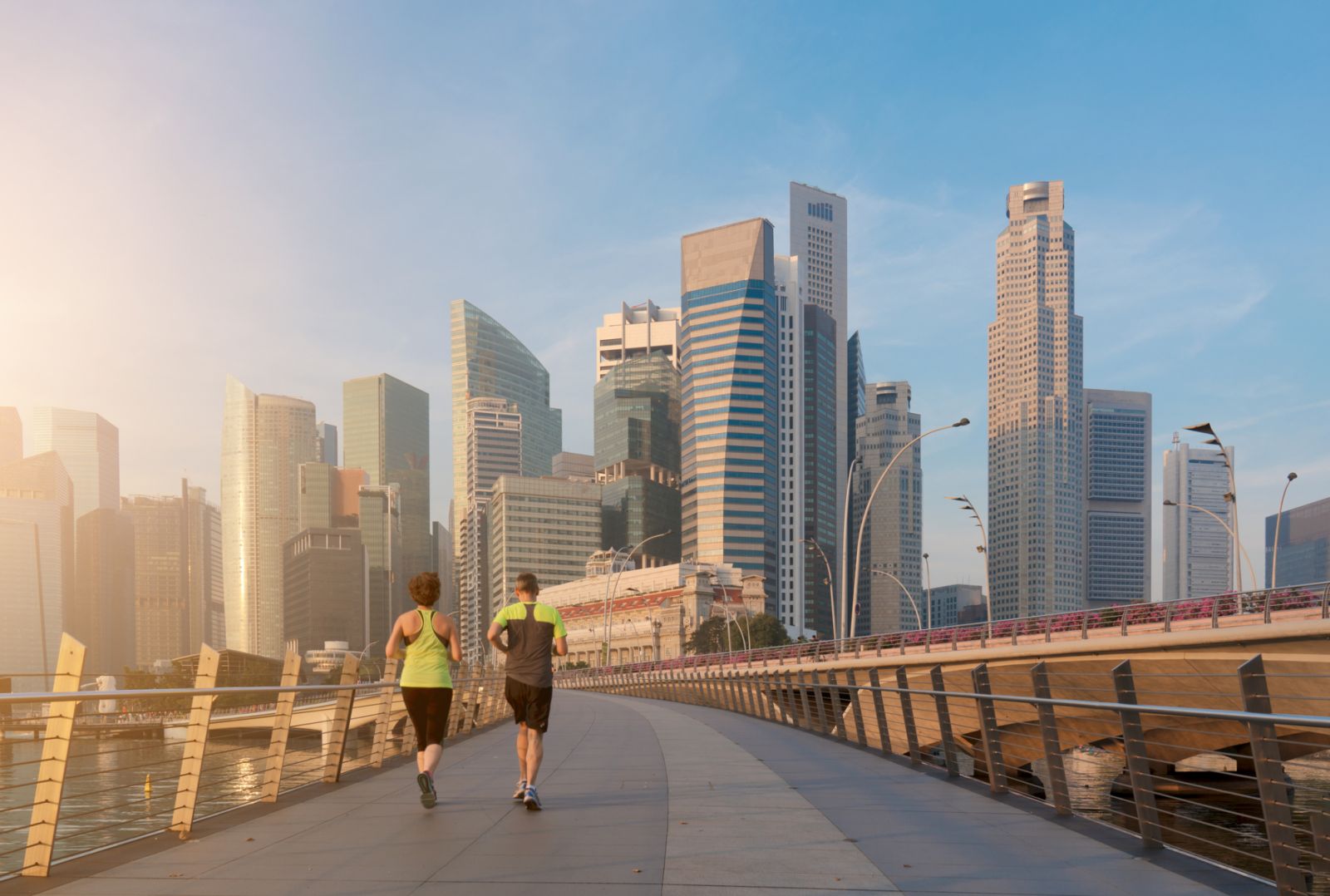 A jogger along the bridge near Marina Bay in Singapore, along with skyscrapers in Singapore and Merlion Park in the background.