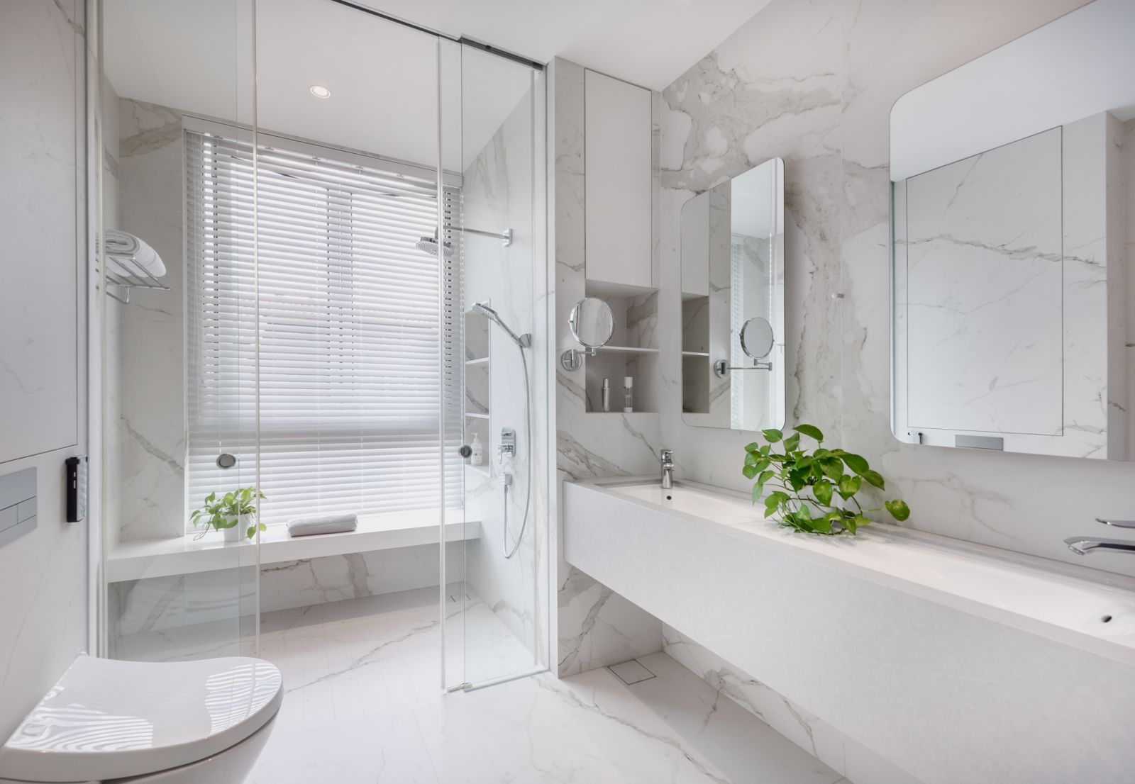 A pristine and luxurious sanctuary with a custom double sink and a bench seat for comfortable showers