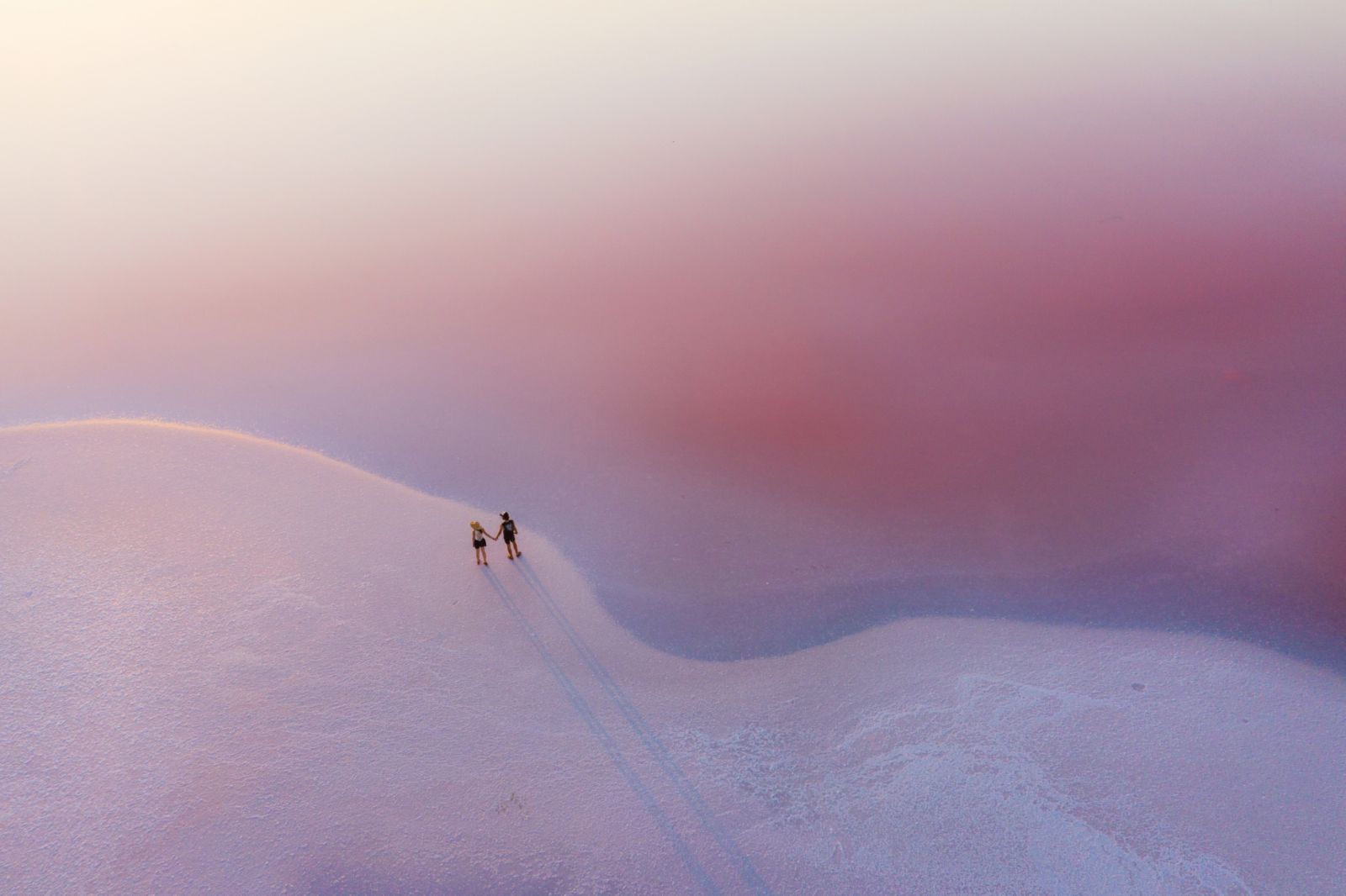 Scenic aerial view of couple walking on pink salt lake