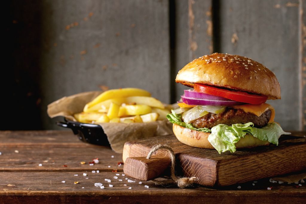 Fresh homemade burger on little cutting board with grilled potatoes. served with ketchup sauce and sea salt over wooden table with gray wooden background. Dark rustic style.. (Photo by: Natasha Breen/REDA&CO/Universal Images Group via Getty Images)