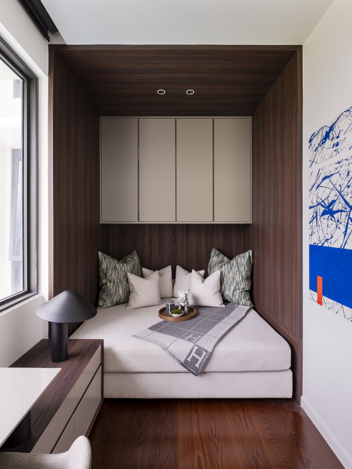 An ingenious reading nook carved into a wood-paneled alcove provides an intimate space for relaxation. The built-in daybed, adorned with an Hermès throw, exemplifies the attention to detail found throughout this residence