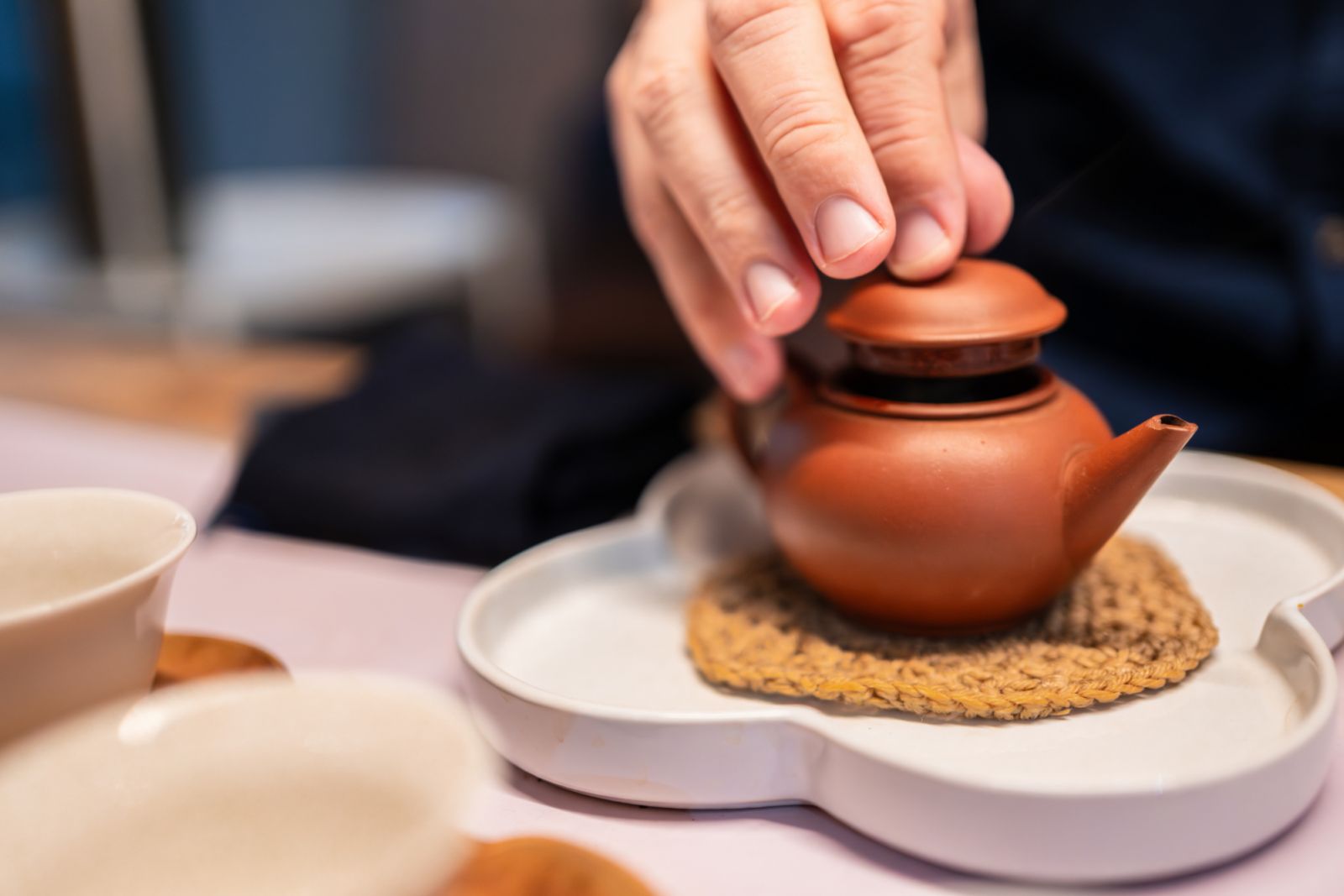 Detail of a hand gently lifting the lid of the teapot, releasing the fragrant aroma of tea.