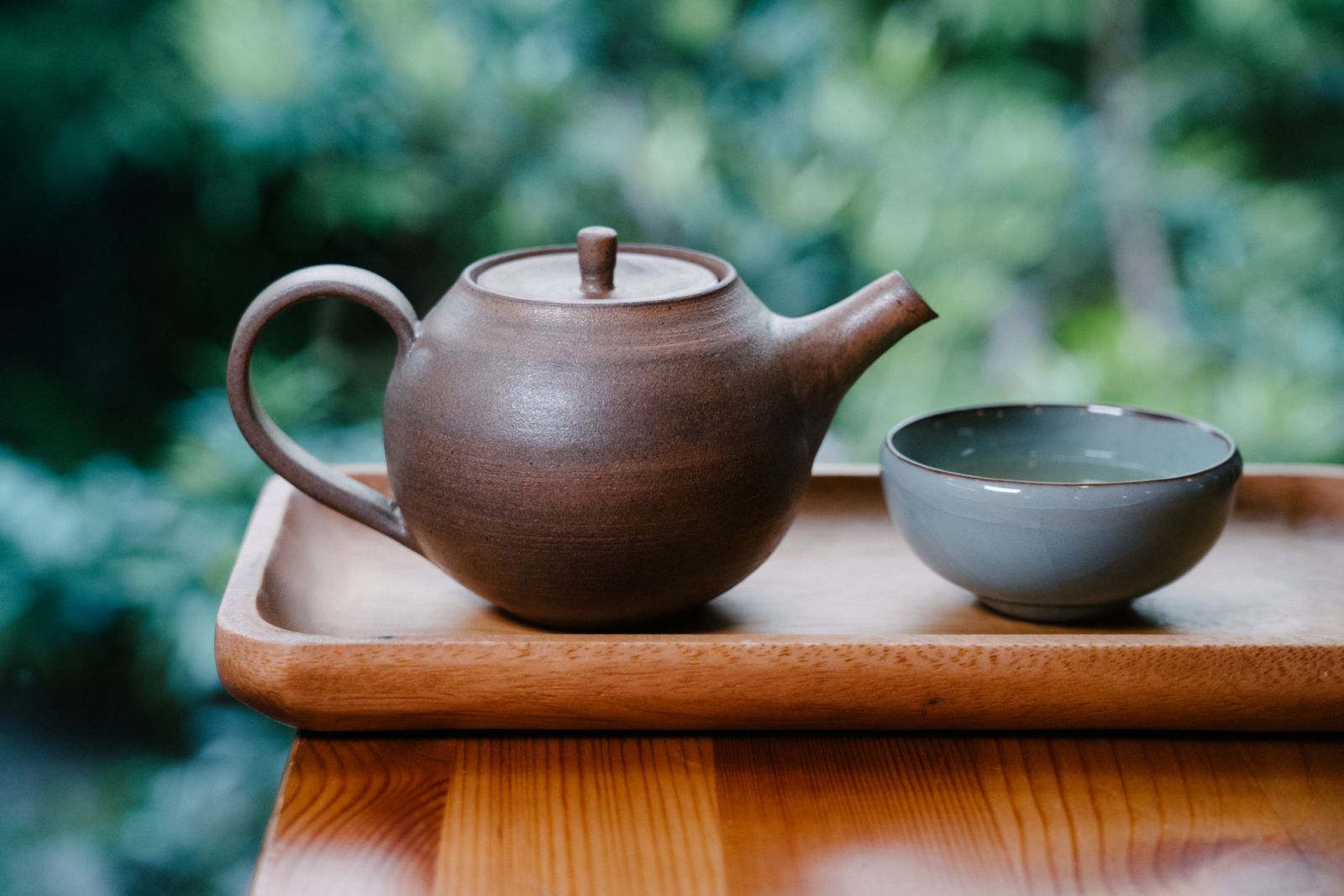 chinese tea pot with glass with green plants in the background