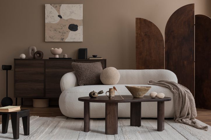 Interior design of cozy living room interior with mock up poster frame, boucle sofa, stylish sideboard, ladder, pouf, books, vase with dried flowers and personal accessories. Home decor. Template.