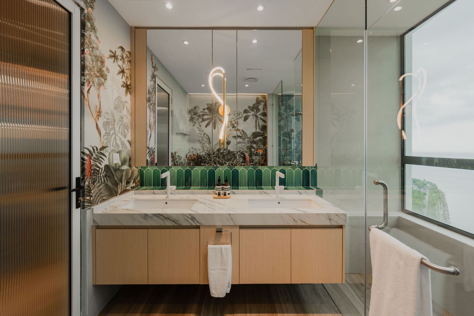 The luxurious bathroom featuring a double vanity with marble countertops, emerald green arch-patterned tile backsplash, and a tropical botanical wallpaper mural