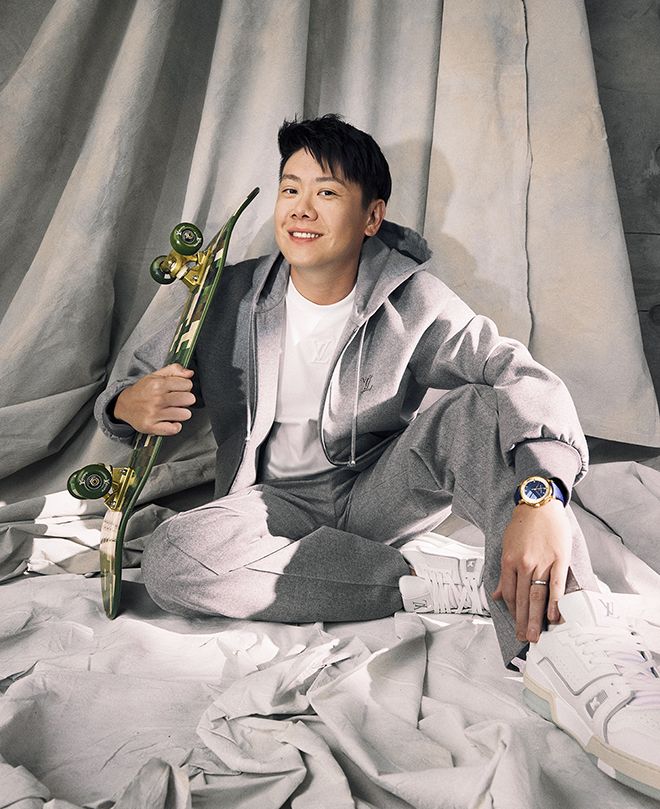 Lai wears Louis Vuitton hoodie, T‑shirt, trousers, and a Escale Automatic 39 mm watch in rose gold, trainers, and holds a Louis Vuitton Damoflage skateboard