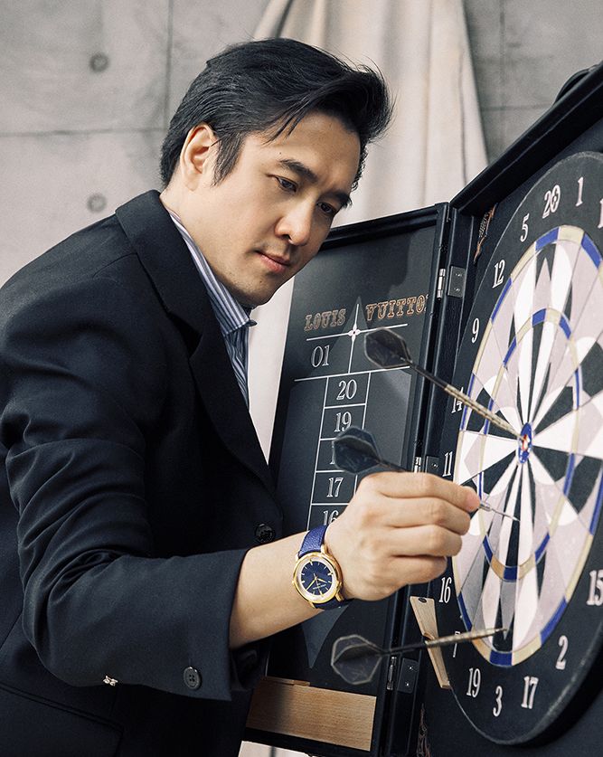 Cheung wears Louis Vuitton jacket, shirt, an Escale Automatic 39 mm watch in rose gold; posing with a Louis Vuitton Dart Trunk LV Dart