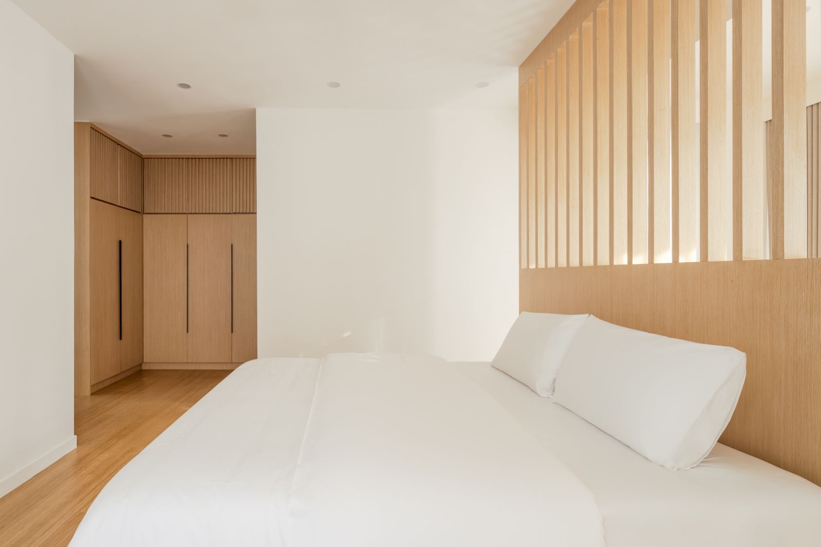 The minimalist bedroom showcases bamboo flooring and custom wood paneling with integrated lighting