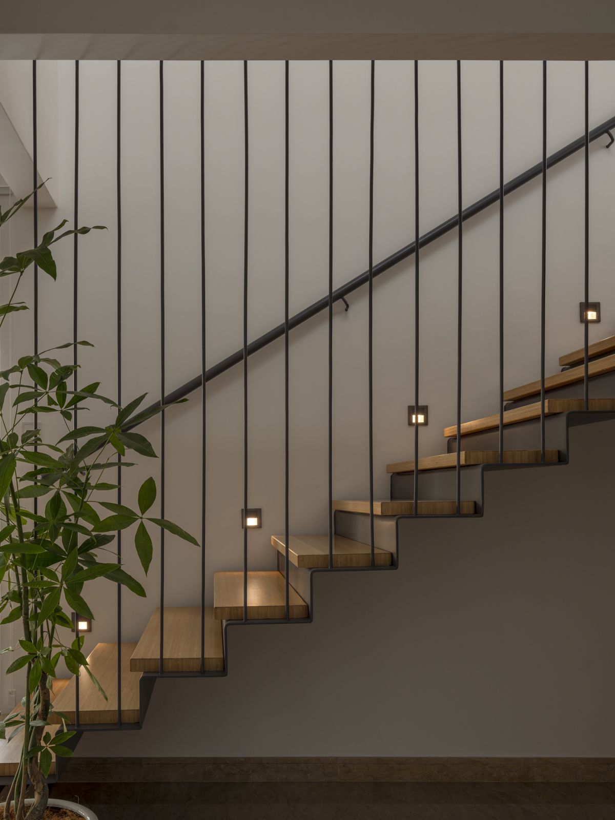 A sculptural staircase featuring bamboo treads and vertical steel elements is illuminated by integrated LED lighting, creating a striking architectural feature in the home’s central space