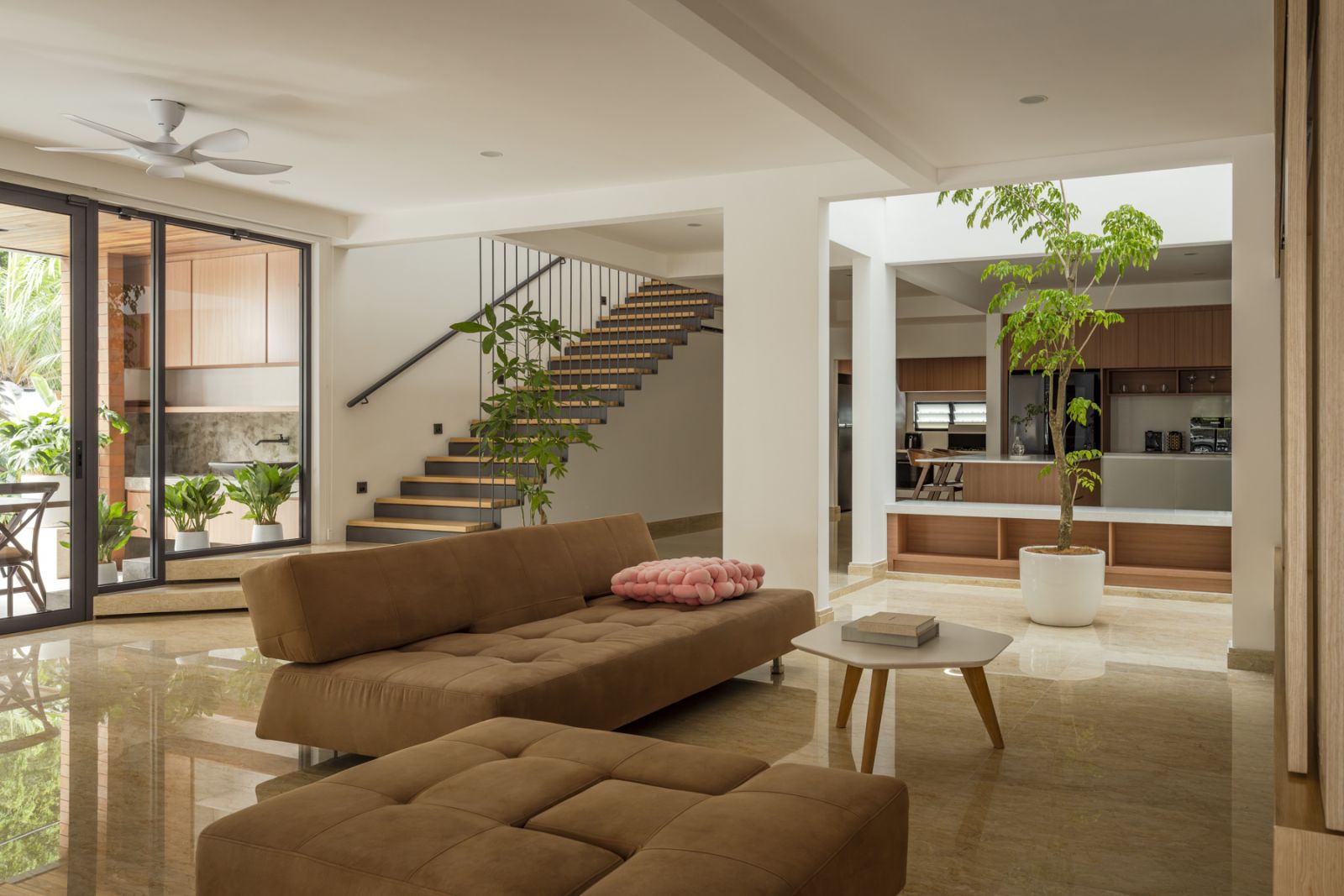 The open-plan living area features polished stone flooring and a brown modular sofa from Long Horn, while sliding glass doors connect to the shaded terrace