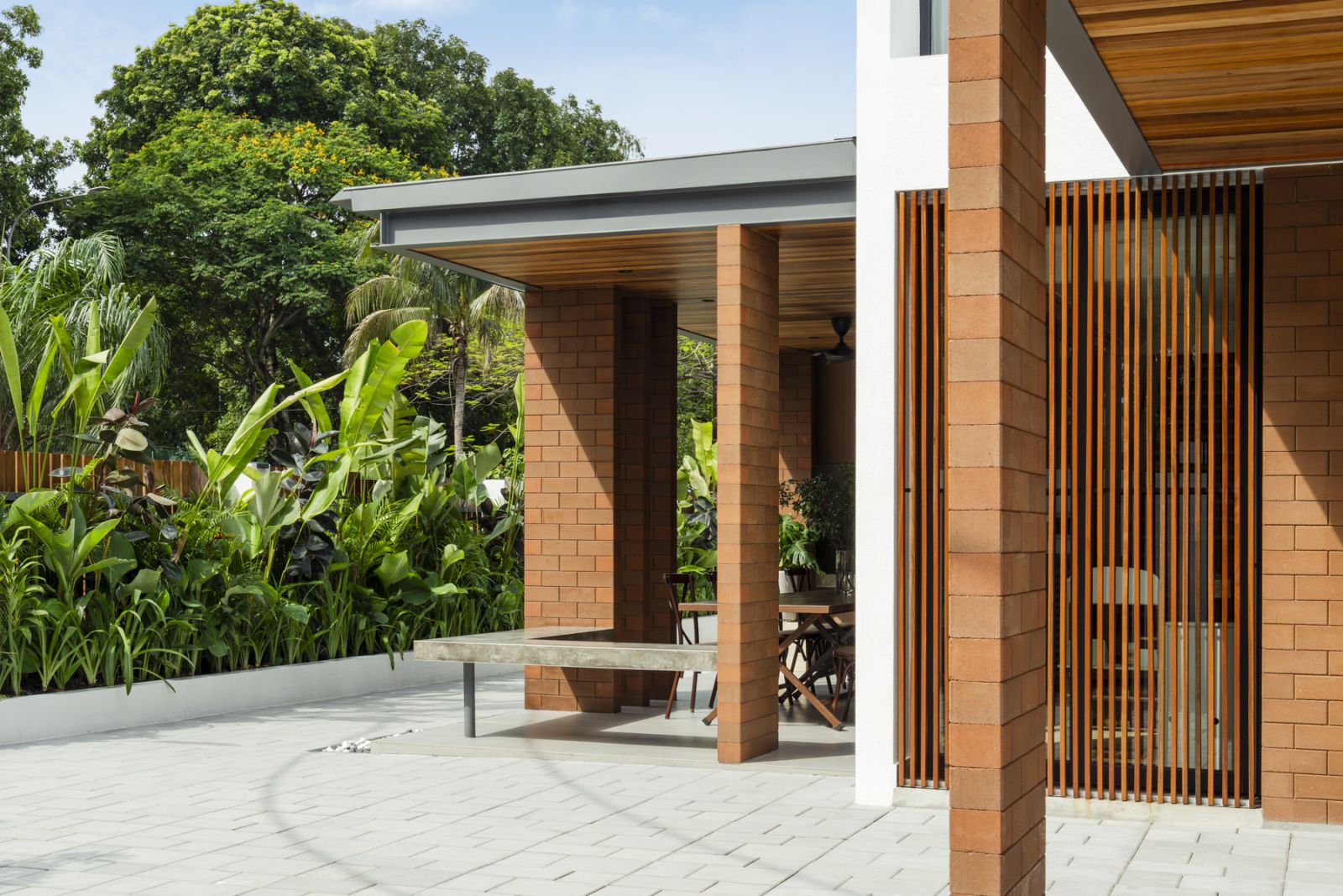 Lush tropical landscaping surrounds the terrace, where terracotta-colored earth brick columns and wooden screens provide privacy while maintaining a connection to nature
