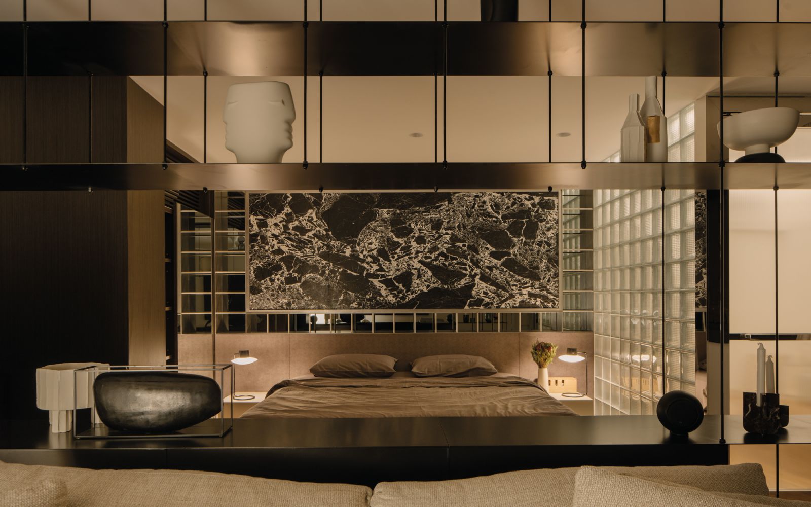 The master bedroom is framed by display shelves in the foreground and a marble slab feature wall in the background