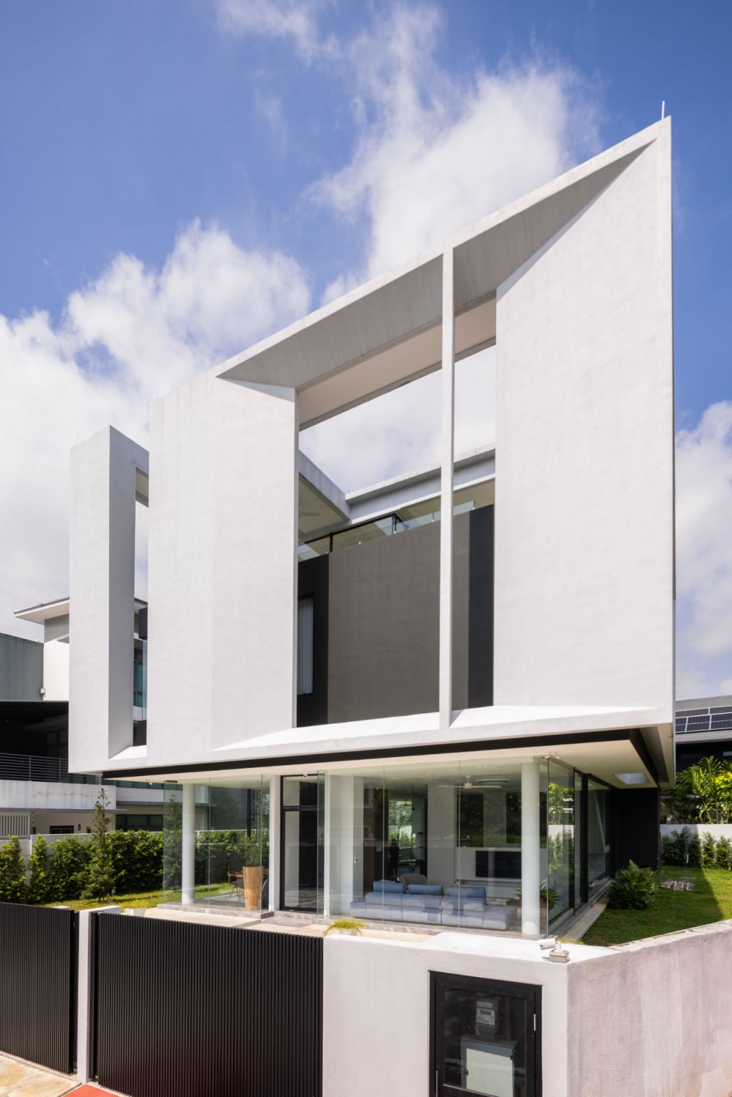 The Float-Box House's distinctive silhouette reveals its dual nature: a transparent ground floor with minimal glass framing creates the illusion of levitation, while the substantial white concrete upper volume appears to hover above the landscaped garden