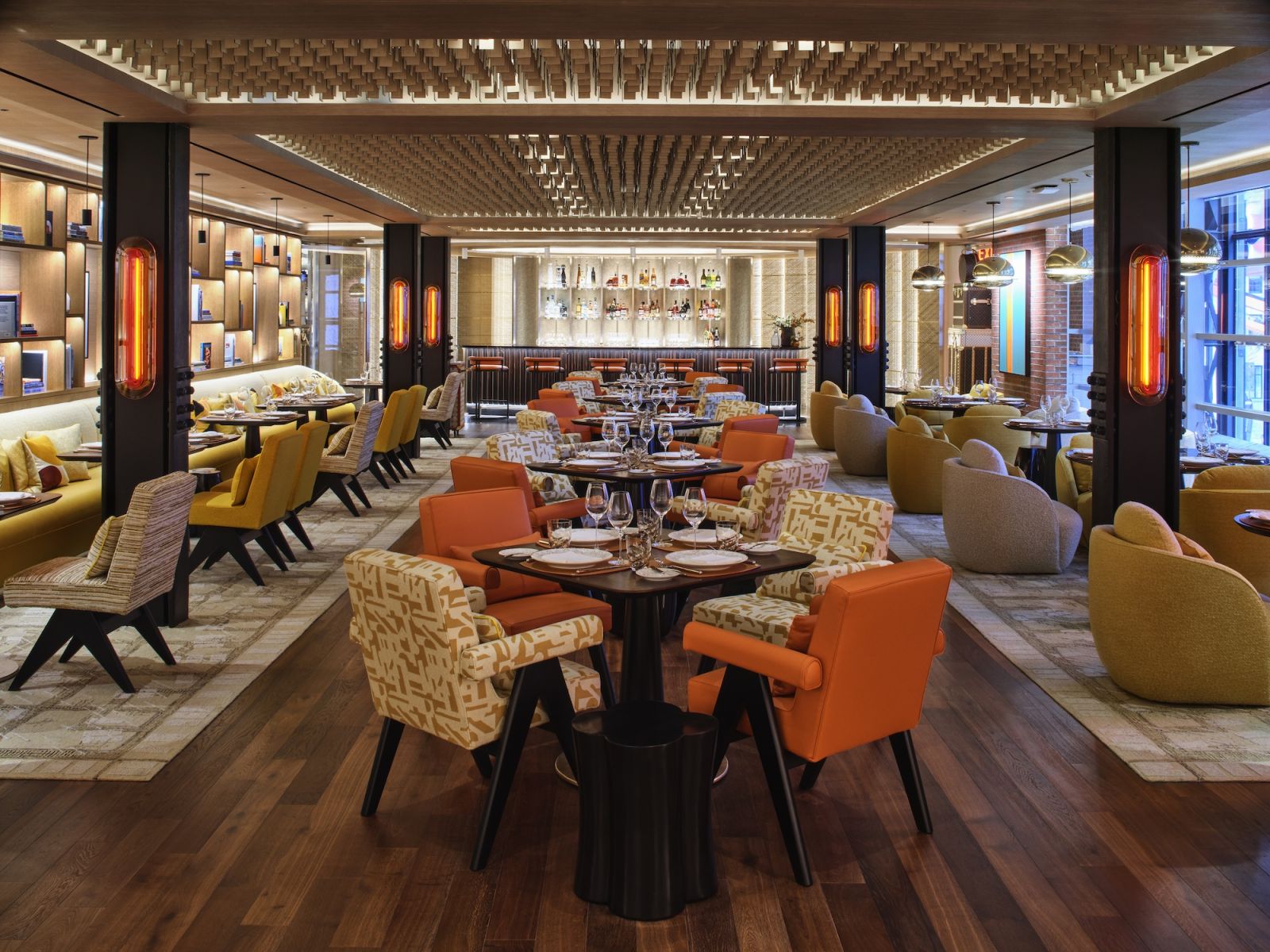 Le Café Louis Vuitton, the brand's first American dining venue, featuring a sophisticated interior with custom lighting, textured ceiling details, and a carefully curated mix of orange, yellow, and neutral-toned furniture
