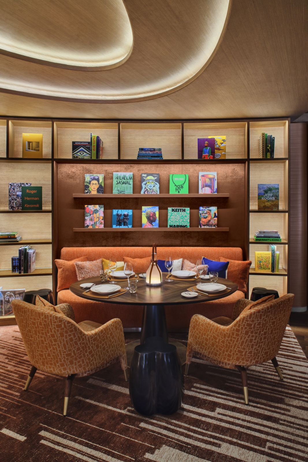 A cosy reading nook within Le Café Louis Vuitton, featuring mid-century inspired furniture in front of the library wall displaying art books including works about Jeff Koons and other contemporary artists who have collaborated with the brand.
