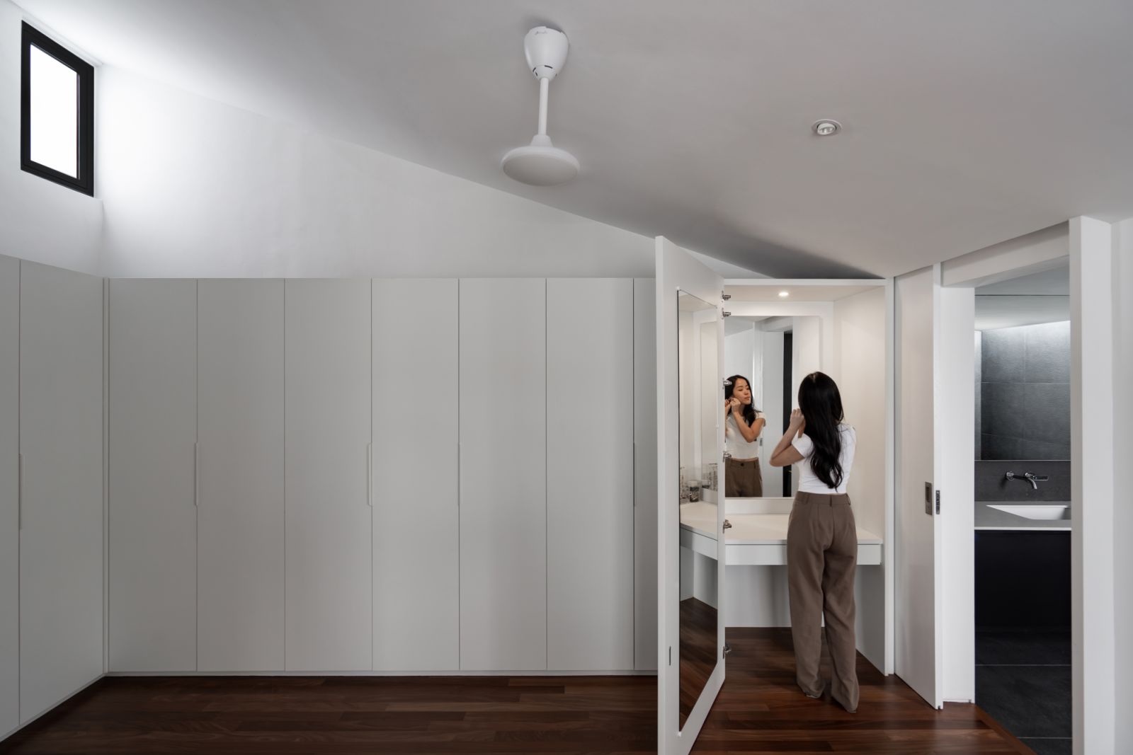 A seamless wall of built-in wardrobes leads to a bright vanity area, exemplifying the home’s thoughtful storage solutions.