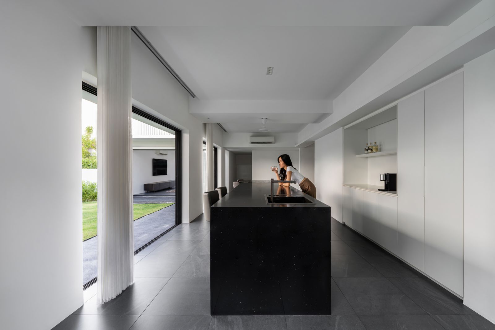 The minimalist kitchen centers around a dramatic black stone island, with floor-to-ceiling sliding doors opening to the garden