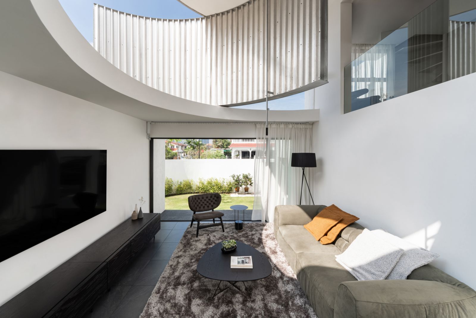 The double-height living room showcases the curved metal wall detail, with a pendant light adding vertical emphasis to the space