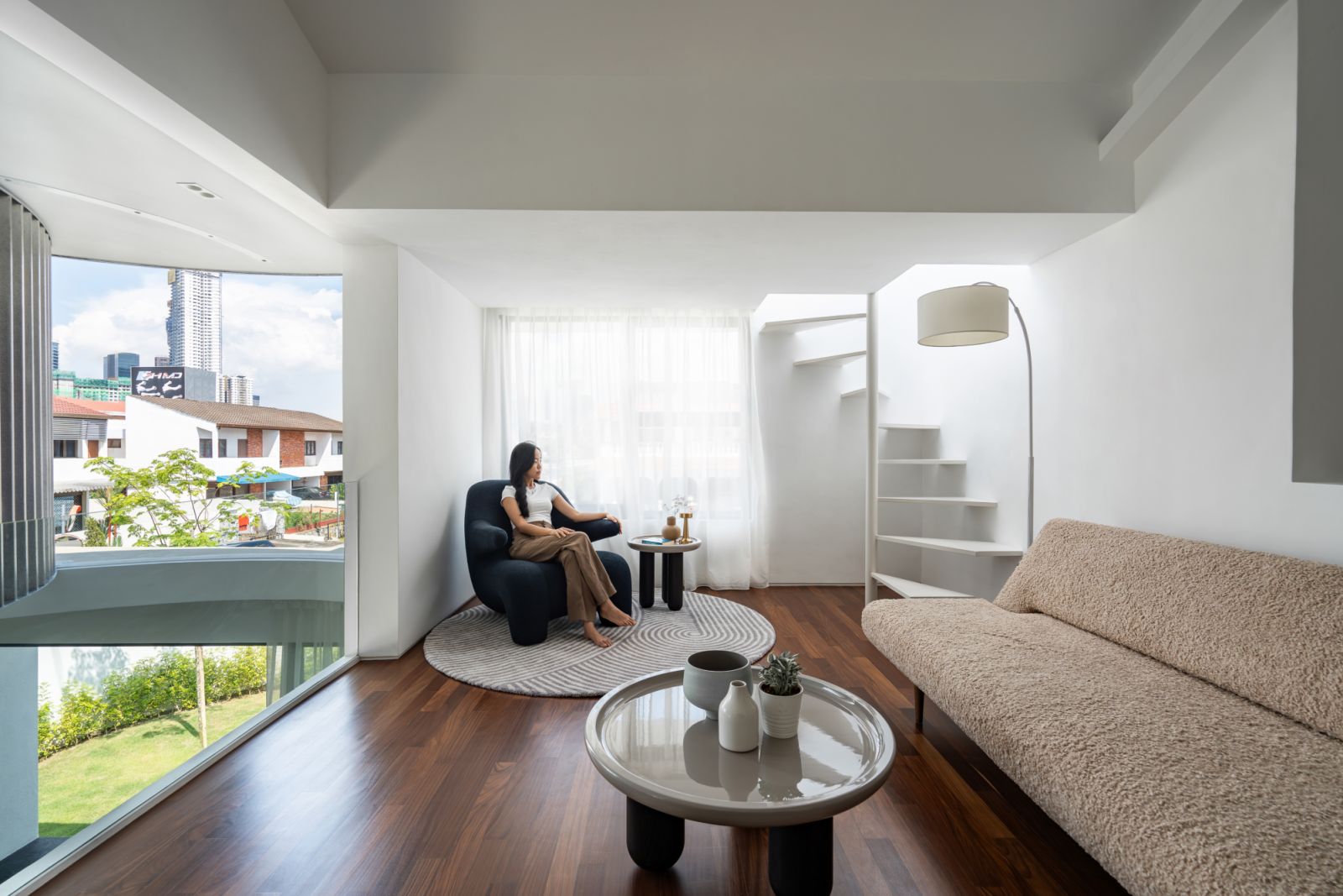 A cosy reading nook offers panoramic views of the Kuala Lumpur skyline, featuring a sculptural black chair and plush sofa next to the staircase leading to the roof