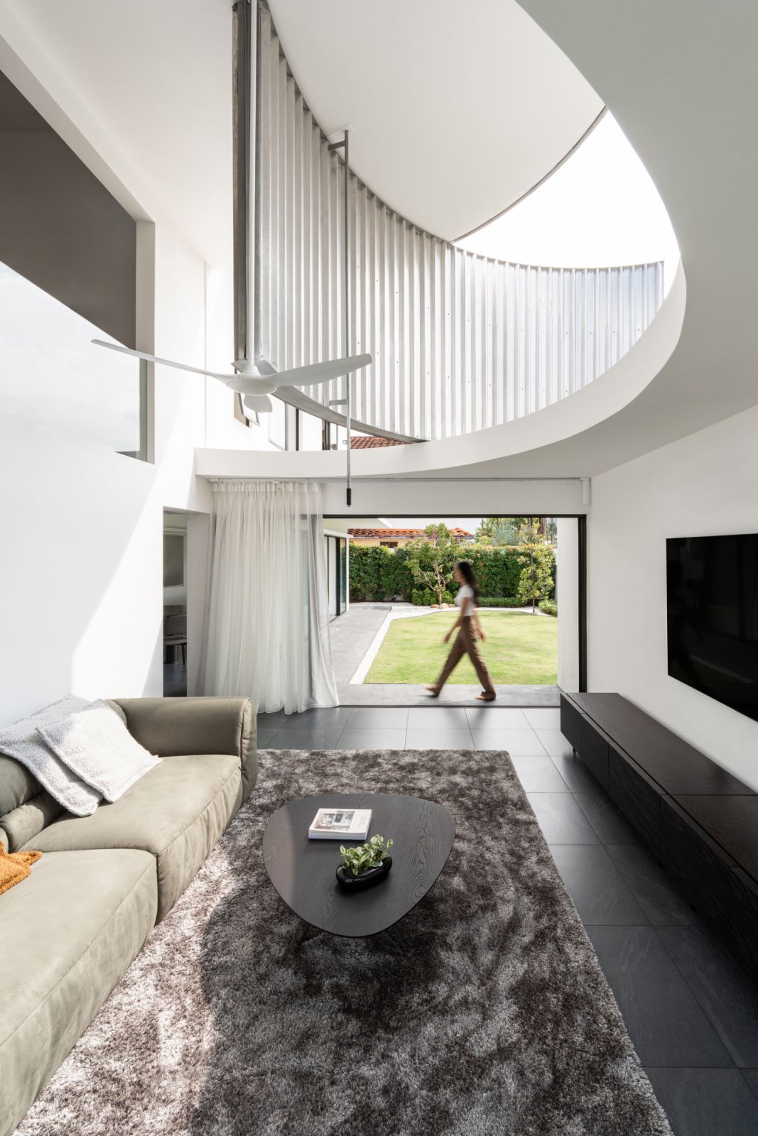 A sage green sofa and plush grey rug create a comfortable seating area that opens directly to the garden through full-height glass doors