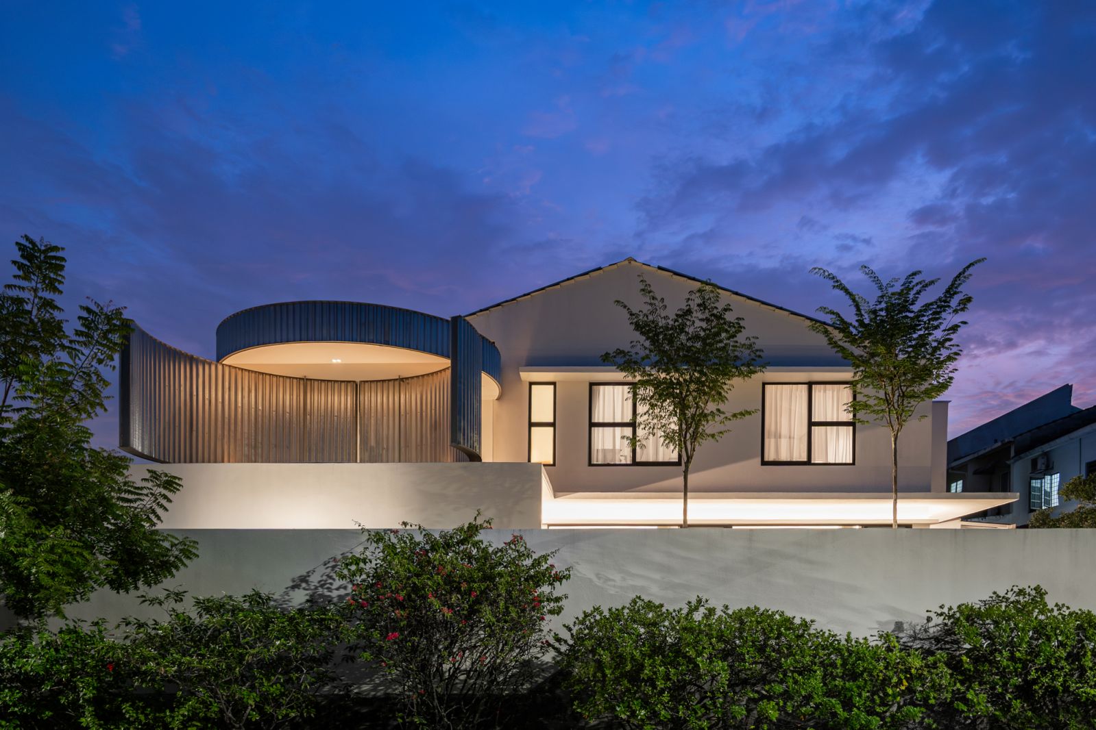 The CC House glows at dusk, with its signature cylindrical metal features illuminated against the purple-blue twilight sky