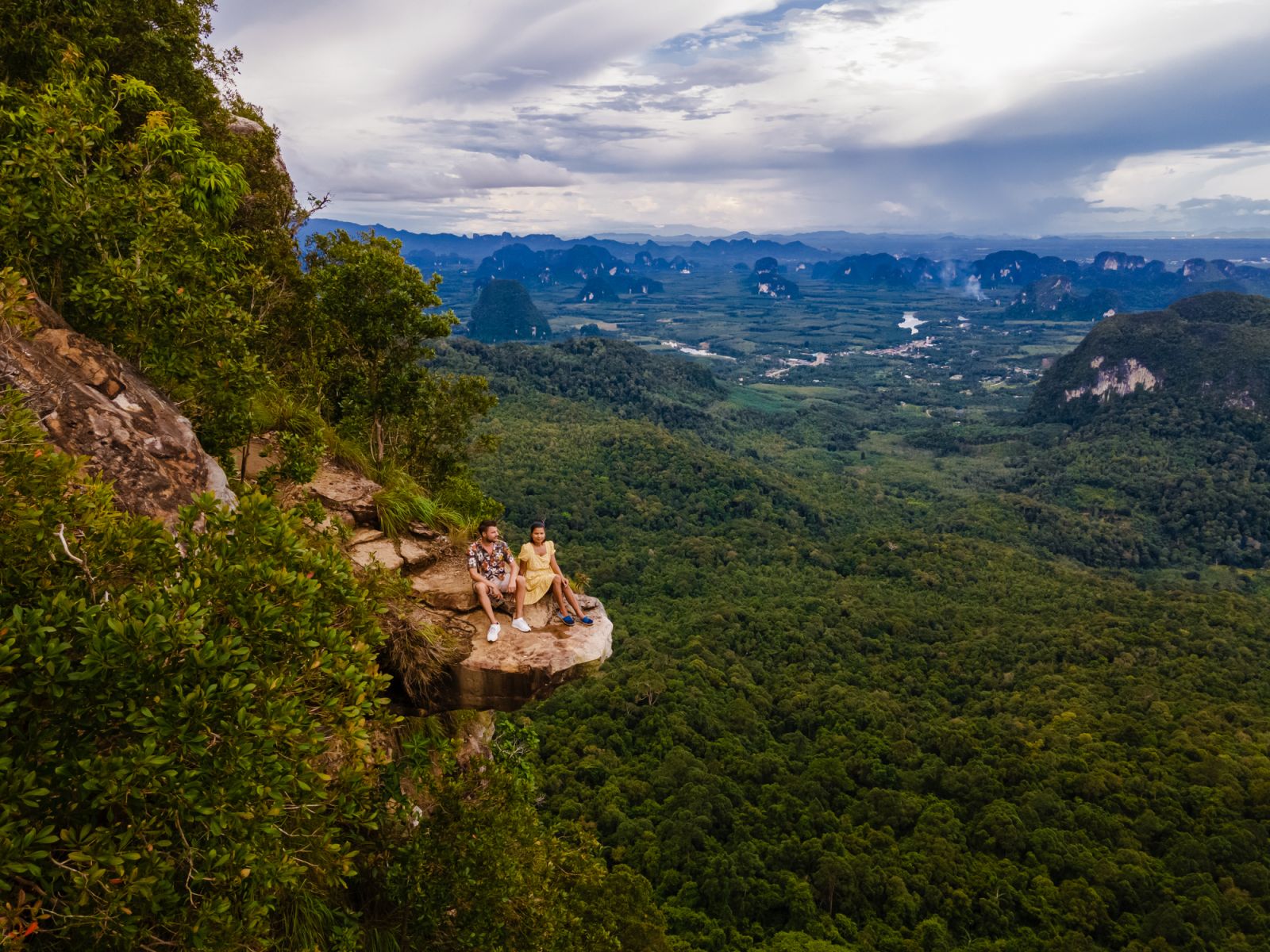 Couple men and women at the edge of a mountain, Dragon Crest mountain Krabi Thailand, Young travelers sits on a rock that overhangs the abyss, Dragon Crest or Khuan Sai at Khao Ngon Nak