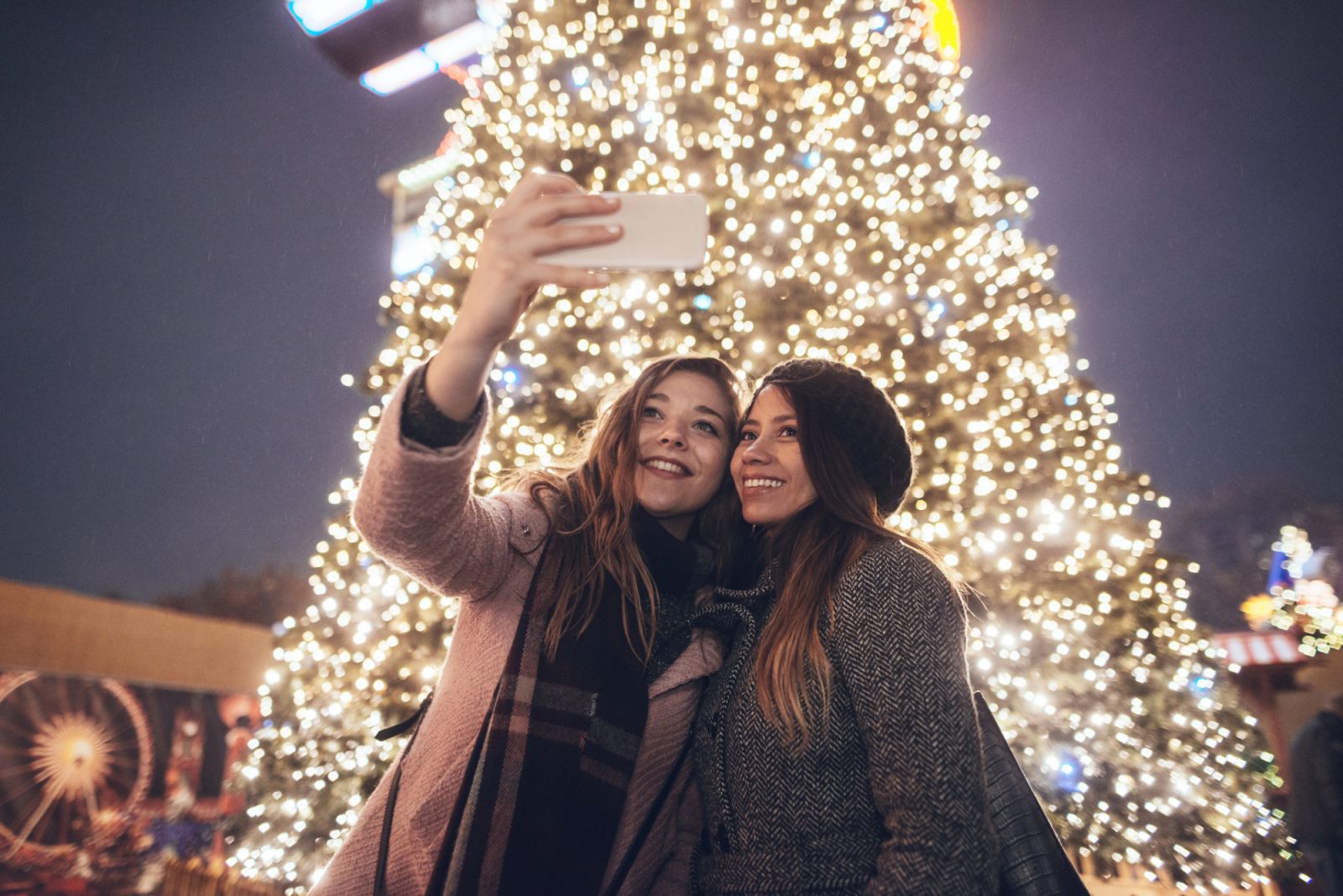Smiling girlfriends taking a selfie on christmas market.