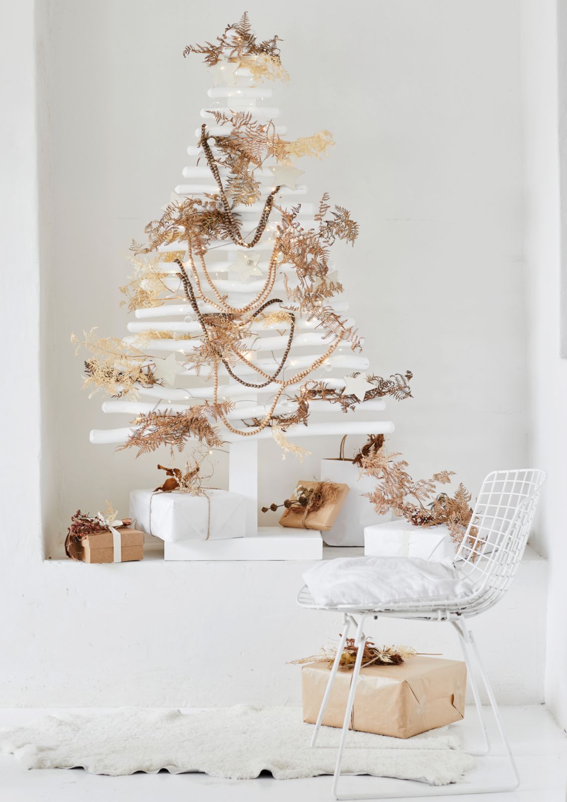 A pared-back, two-dimensional Christmas “tree” made from branches painted in snowy white and layered with wooden beads and fairy lights