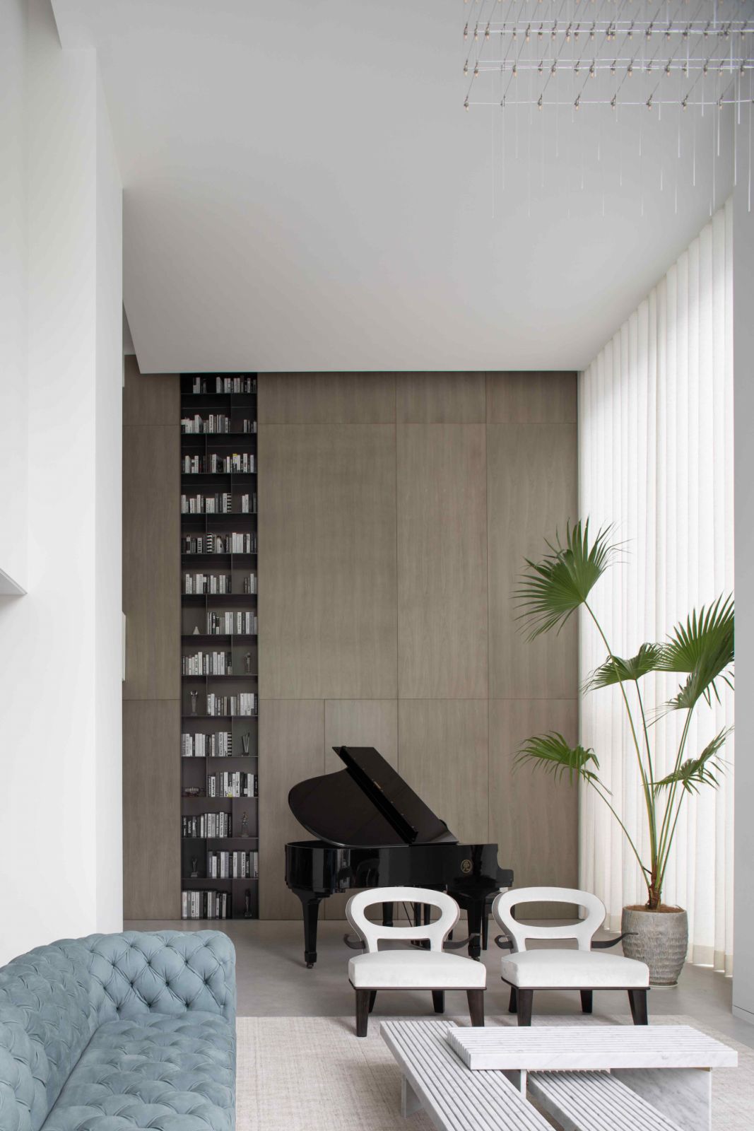 A grand piano against the backdrop of grey stone-clad wall panels and a black double-height open bookshelf