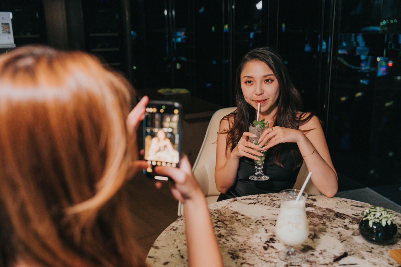 Happy Generation Z girls tavelling in Zhuhai, Greater Bay Area, China, enjoying snacks and drinks at a bar in the hotel, taking some photos
