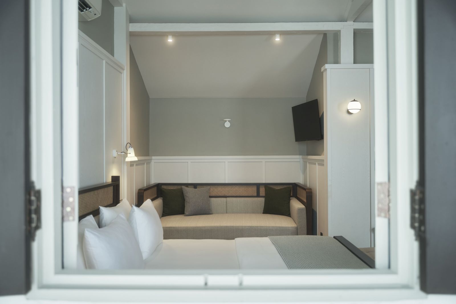 A glimpse through louvred windows reveals Studio 11’s refined renovation of the Mews rooms, where olive green accents and rattan details complement the serene neutral palette