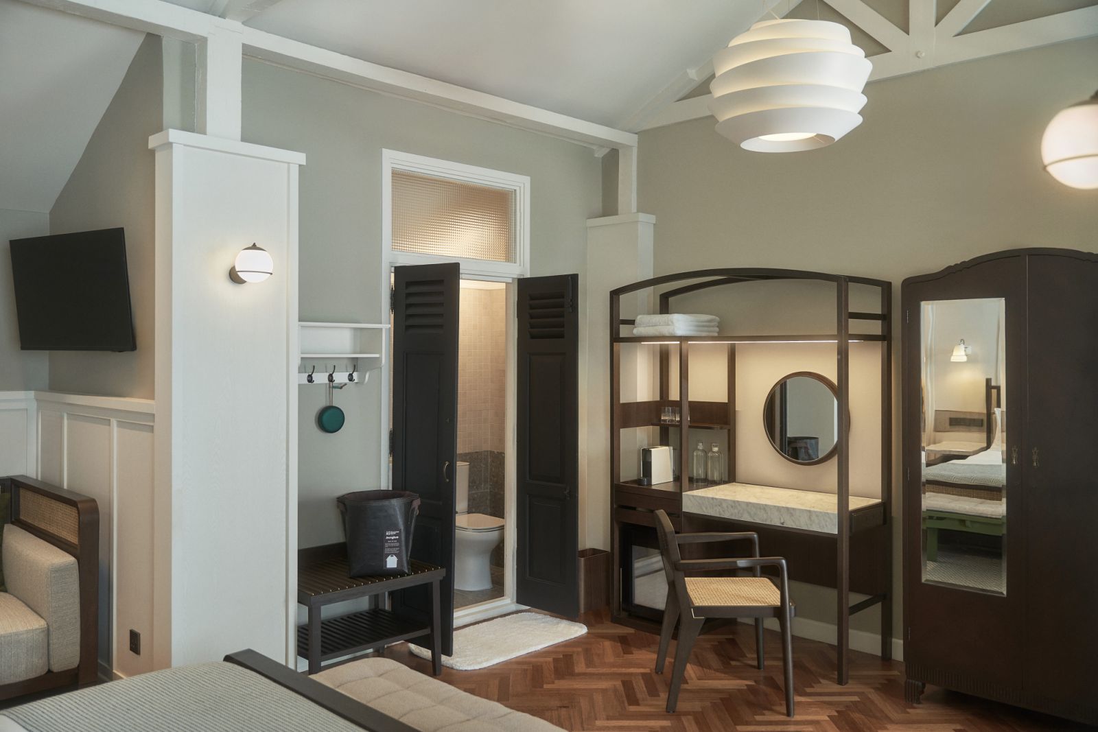 Thoughtful design elements converge in the Mews rooms: herringbone parquet flooring, contemporary rattan furniture, traditional black shutters, and modern amenities like the Le Soleil pendant light, creating a sophisticated dialogue between old and new