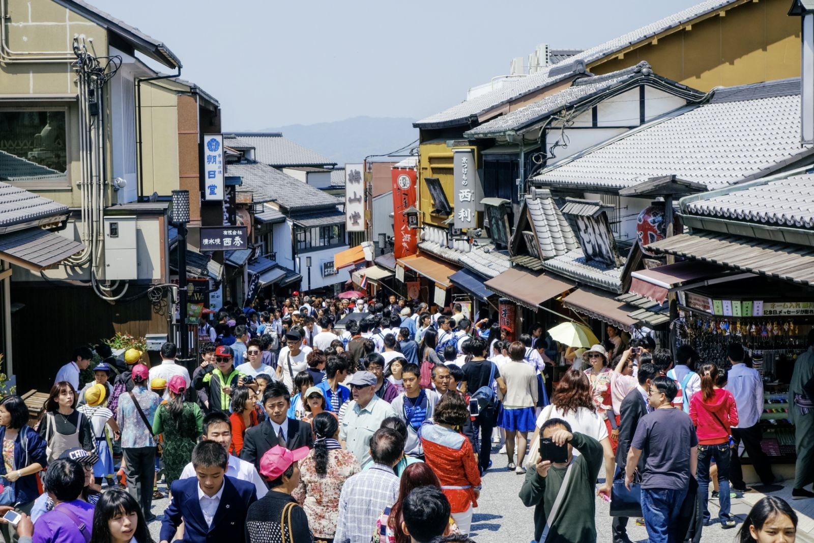 A view of a busy street in Kyoto. Shopping district, crowded with shoppers and tourists. Daytime, people, horizontal composition.