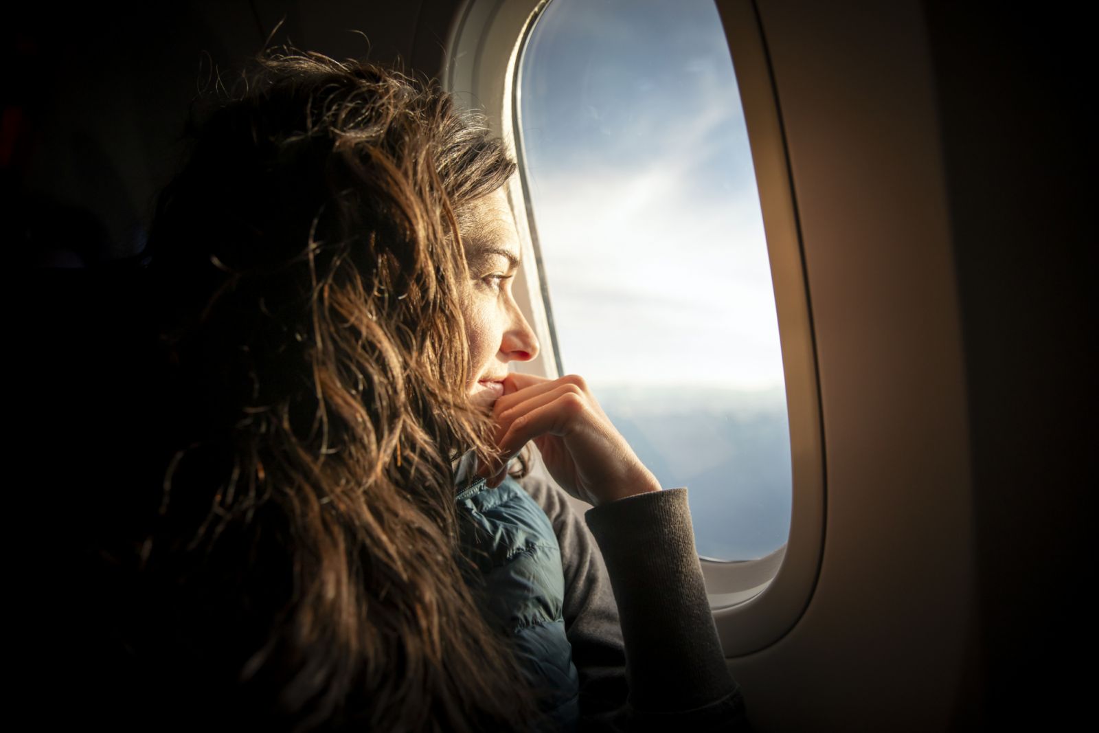A woman looking out of an airplane window at sunrise.