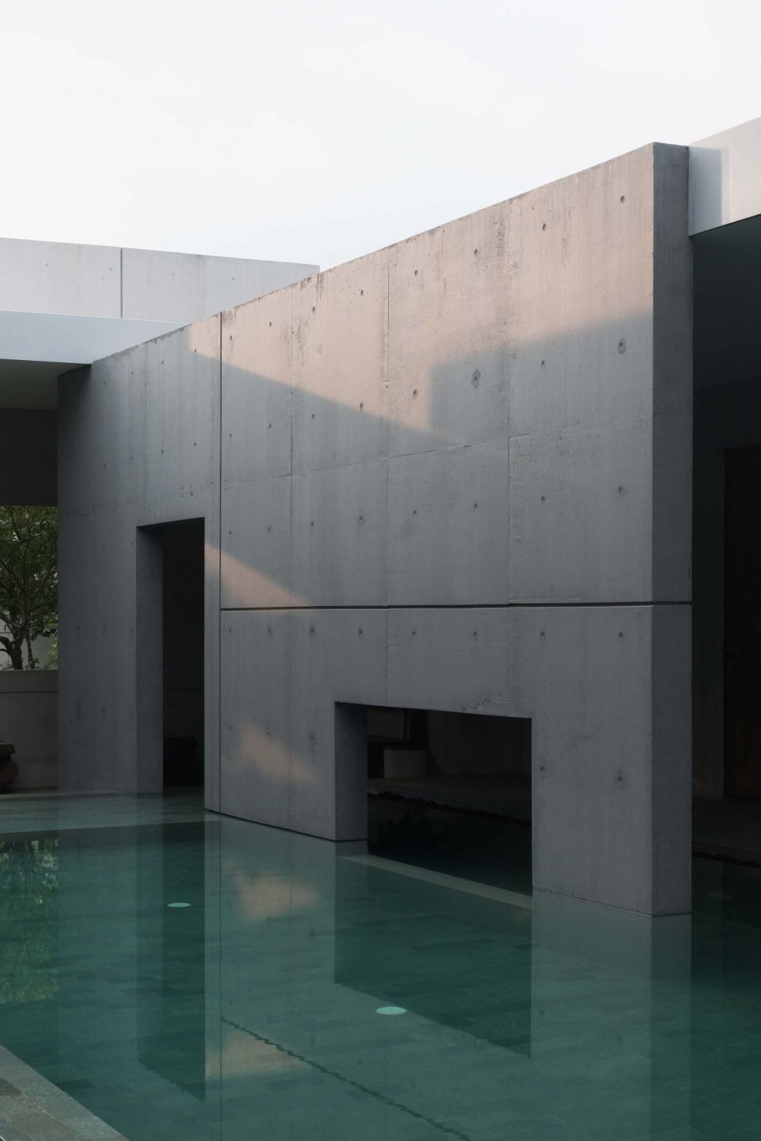 A study in modernist geometry, the poolside concrete planes cast dramatic shadows across their bare surfaces, while geometric cutouts create depth and intrigue