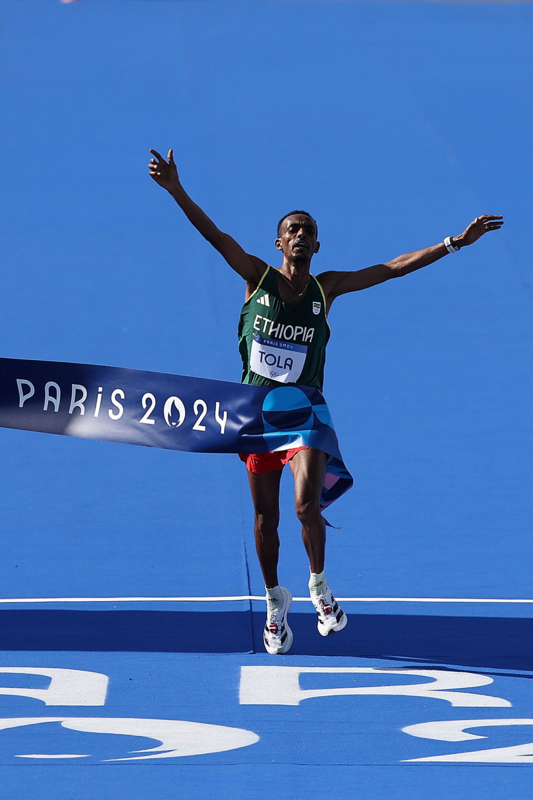 PARIS, FRANCE - AUGUST 10: Tamirat Tola of Team Ethiopia crosses the finish line to win the Gold medal and to break the Olympic Record during the Men's Marathon on day fifteen of the Olympic Games Paris 2024 at Esplanade Des Invalides on August 10, 2024 in Paris, France. (Photo by Hannah Peters/Getty Images)