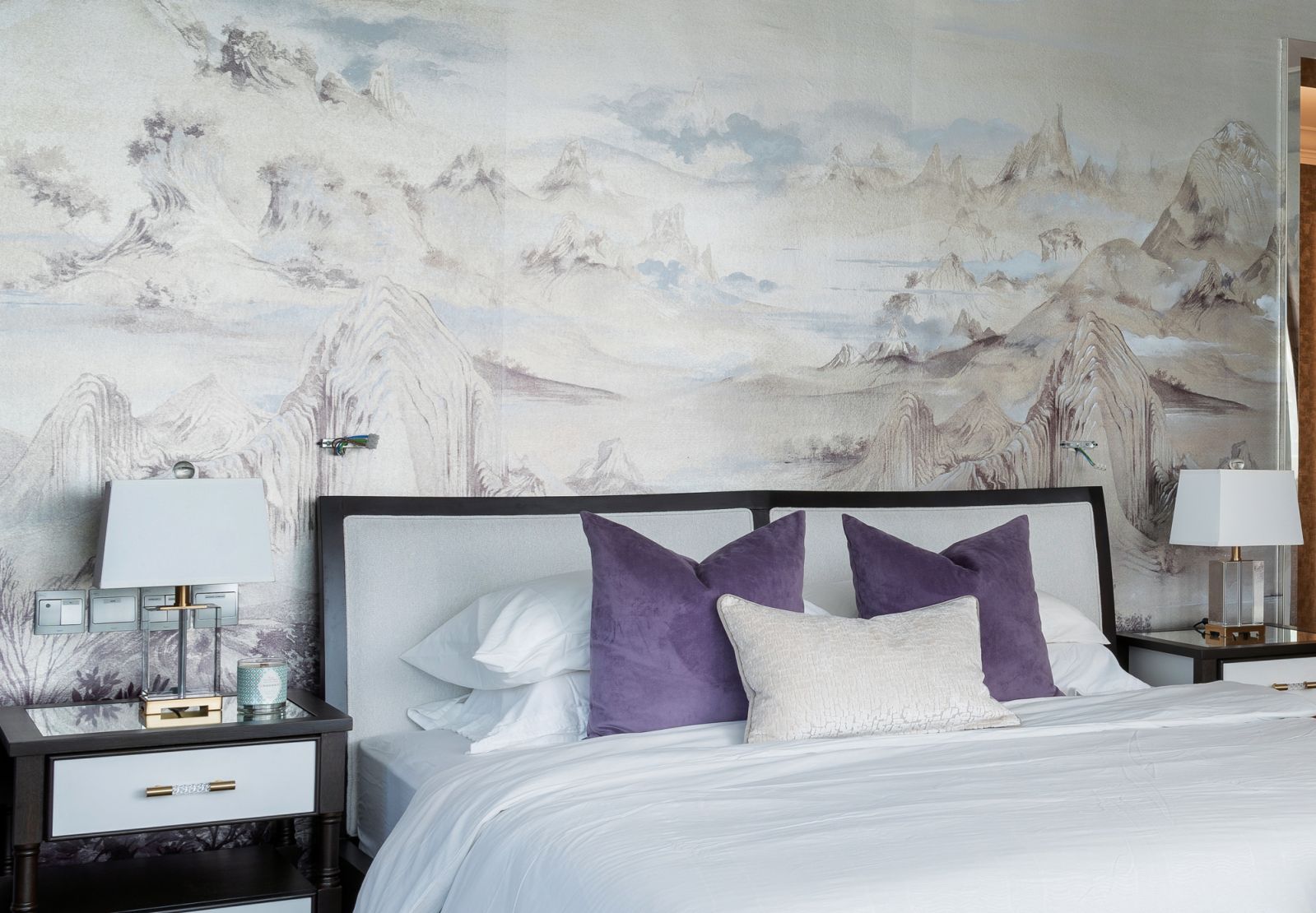 An ethereal wallcovering depicting a misty mountain range and soft furnishings in a deep lilac tone bring a serene quality to the master bedroom