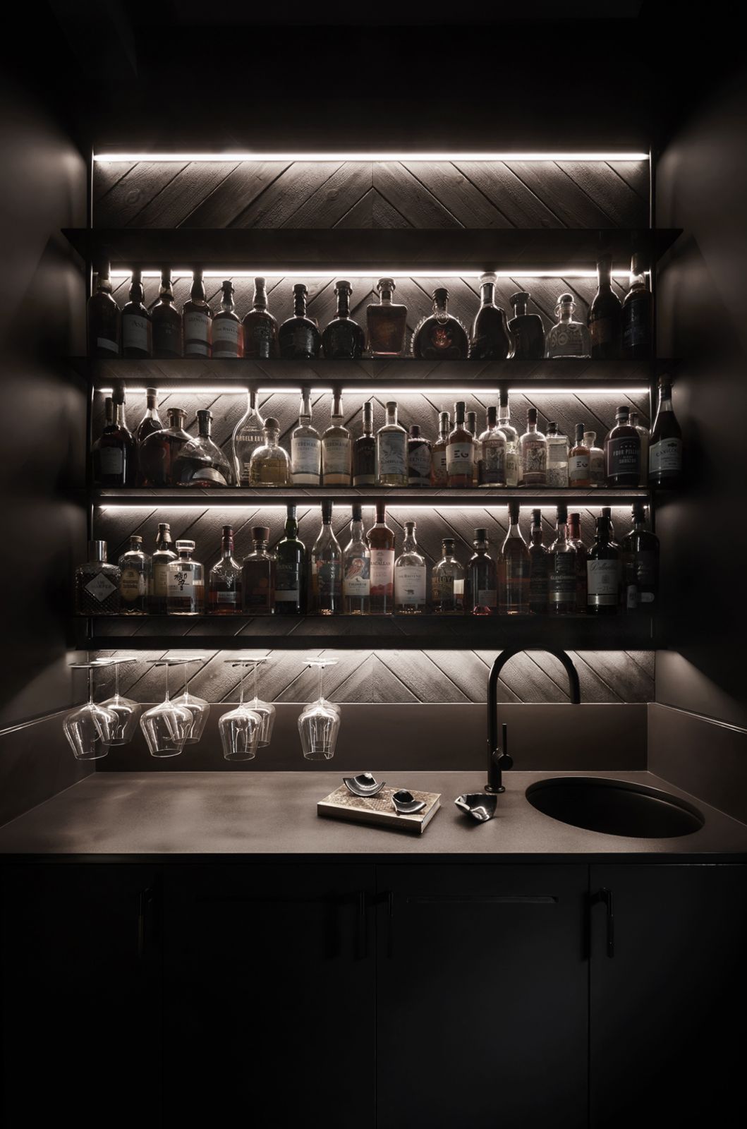 The walk-in bar nestled in the corridor leading to the entertainment room is revealed through illuminated smoked glass walls