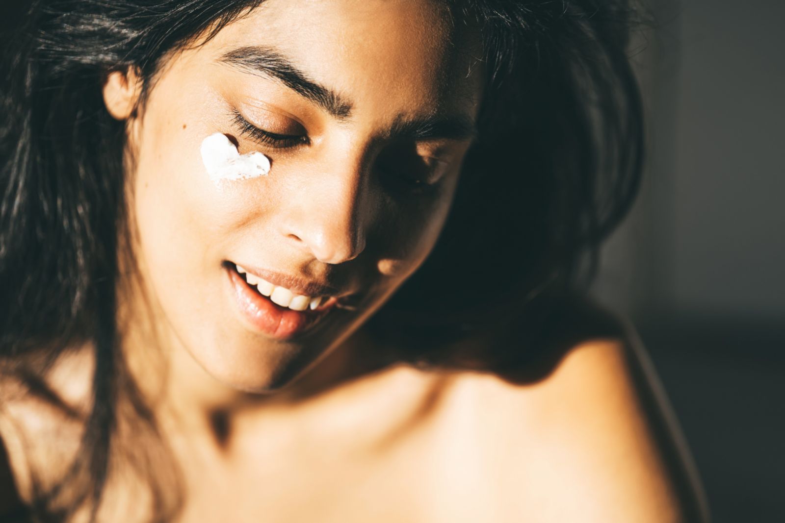 A beautiful Asian woman enjoying a morning skincare routine, applying a sunblocking moisturizer to her skin. She is smiling in the sun with her eyes closed. Concepts of no-makeup, notox, natural beauty, psychodermatology, and anti-aging SPF products to target UV damage and prevent sun damage. Versatile, functional gender-neutral products are the future of science-based personalized skin care and cosmetology, products carefully selected for specific skin types with AI technology.