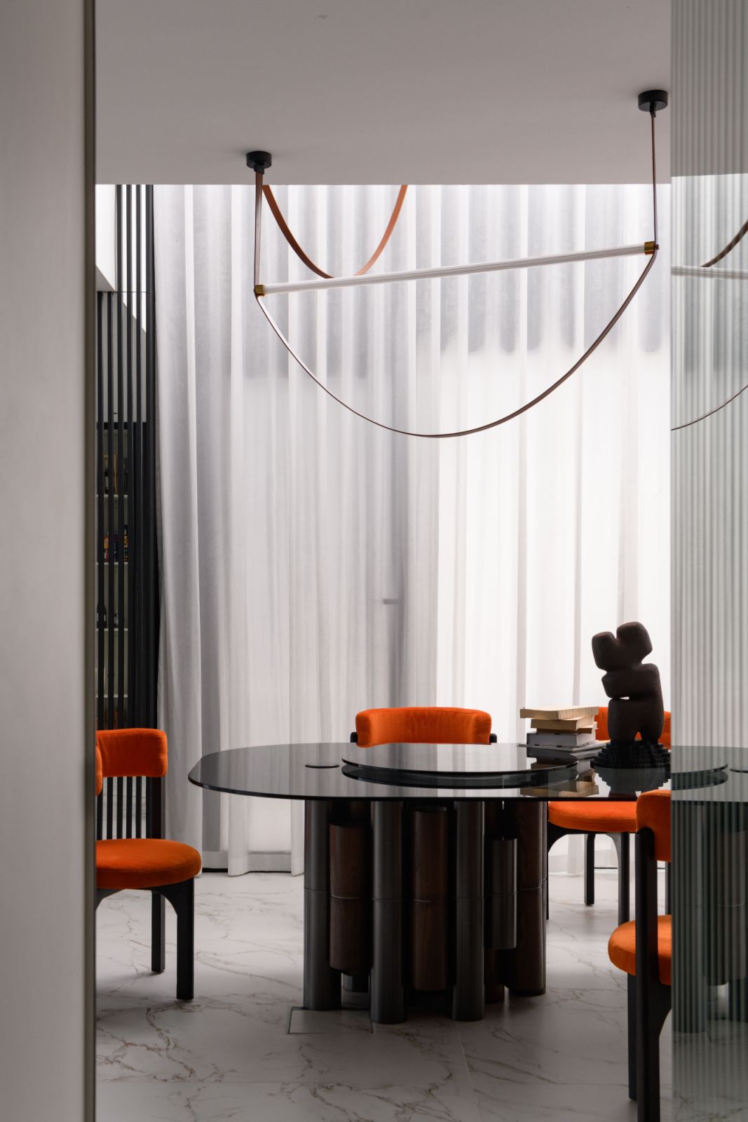 The dining space flows seamlessly into the living room and kitchen along a single axis, featuring a custom glass-topped table