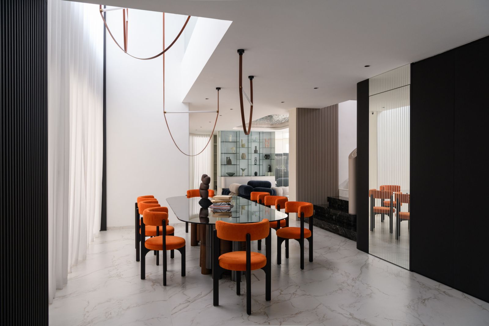 The dining space flows seamlessly into the living room and kitchen along a single axis, featuring a custom glass-topped table