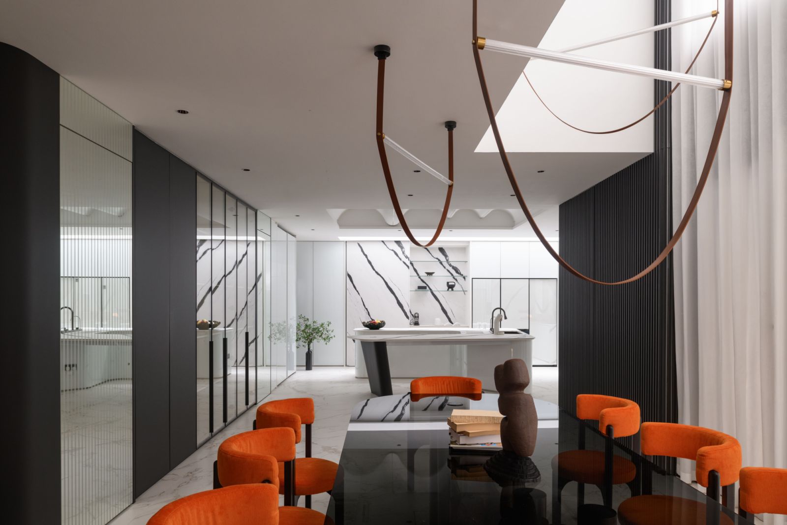 The dining space flows seamlessly into the living room and kitchen along a single axis, featuring a custom glass-topped table